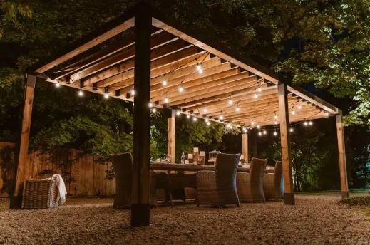 Outdoor dining area under a pergola with string lights at night.
